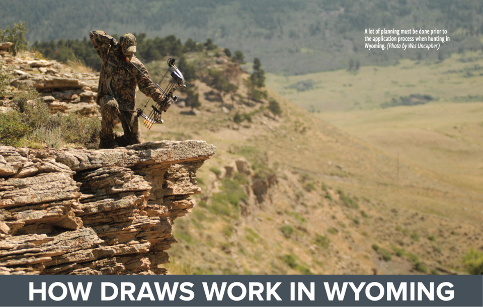 An archery hunter draws his bow from a rocky outcropping