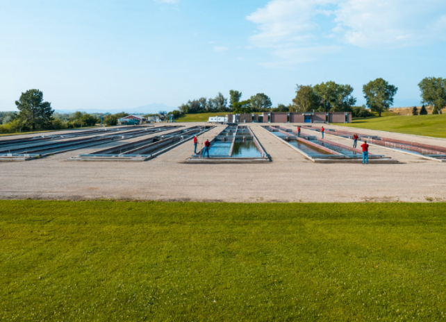 A wide angle photo of the concrete raceways outside of the Clark's Fork Fish Hatchery on a sunny day.
